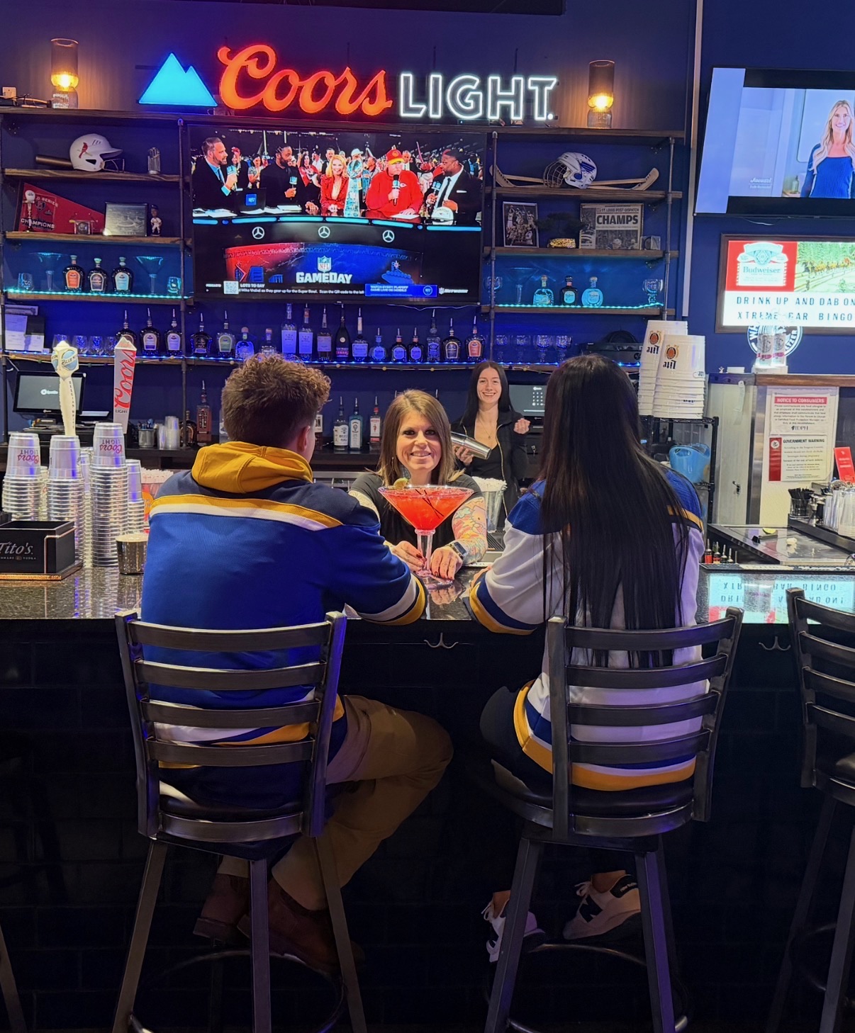 Friends in St. Louis Blues jerseys cheers a fresh cocktail at the Penalty Box bar